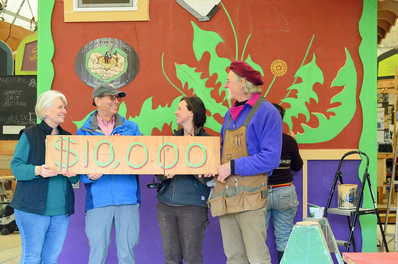 To mark the Rotary Club of Port Townsend’s $10,000 gift to the Community Boat Project — which is constructing tiny homes for local farmworkers — boat project director Wayne Chimenti, far right, and shop organizer Gillian Kenagy, second from right, quickly painted a “check” on a piece of wood. Rotarian Carla Caldwell, far left, and club president Jim Cunnington were among the volunteers who joined a work party toward finishing the project’s latest wooden tiny house last week. (Diane Urbani de la Paz/Peninsula Daily News)