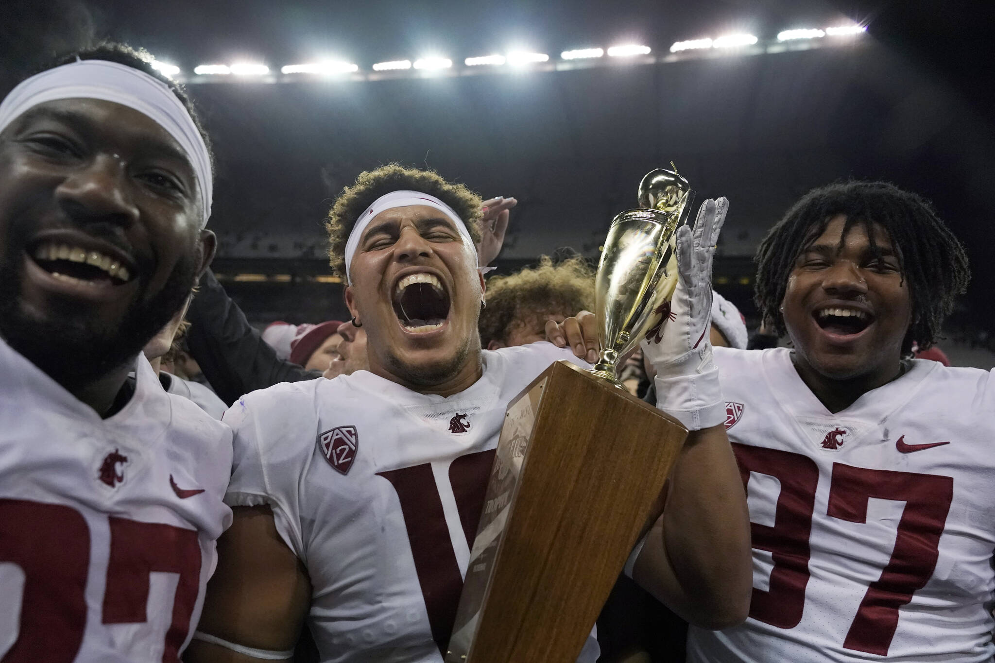 Washington State defensive end Ron Stone Jr., center, celebrates with Willie Taylor III, left, and defensive lineman Ty Garay-Harris, right, as he holds the Apple Cup Trophy after WSU beat Washington 40-13 in an NCAA college football game, Friday, Nov. 26, 2021, in Seattle. (AP Photo/Ted S. Warren)