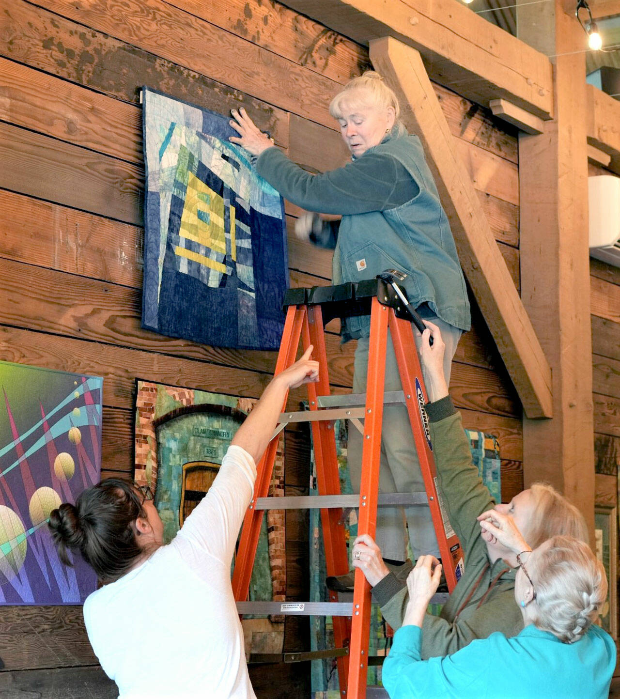 Erica Iseminger of Chimacum, on the ladder, hangs a piece at the Mead Werks with help from Erika Wurm, left, of Port Townsend, Jeri Auty, of Port Ludlow and Caryl Fallert-Gentry of Port Townsend.