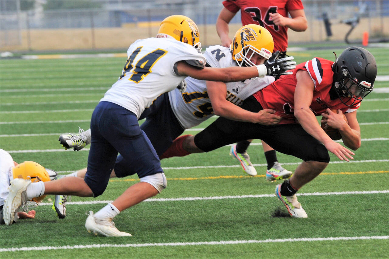 Neah Bay quarterback Julian Carrick is brought down by Naselle’s Jack Strange (44) and Kolten Linstrom (14) on Saturday in Forks. Neah Bay shocked the powerhouse Comets 58-20. (Lonnie Archibald/for Peninsula Daily News)