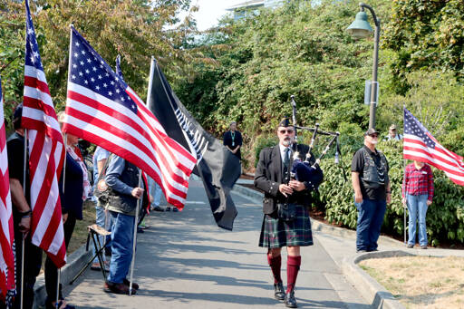 Rick McKenzie starts Sunday’s ceremony at the 9/11 Memorial Park with bagpipe music, walking down the line of flags to the memorial of a 9-foot I-beam from the Twin Towers in New York. About 2,000 of these memorial pieces of wreckage have been placed around the country. (Dave Logan/for Peninsula Daily News)