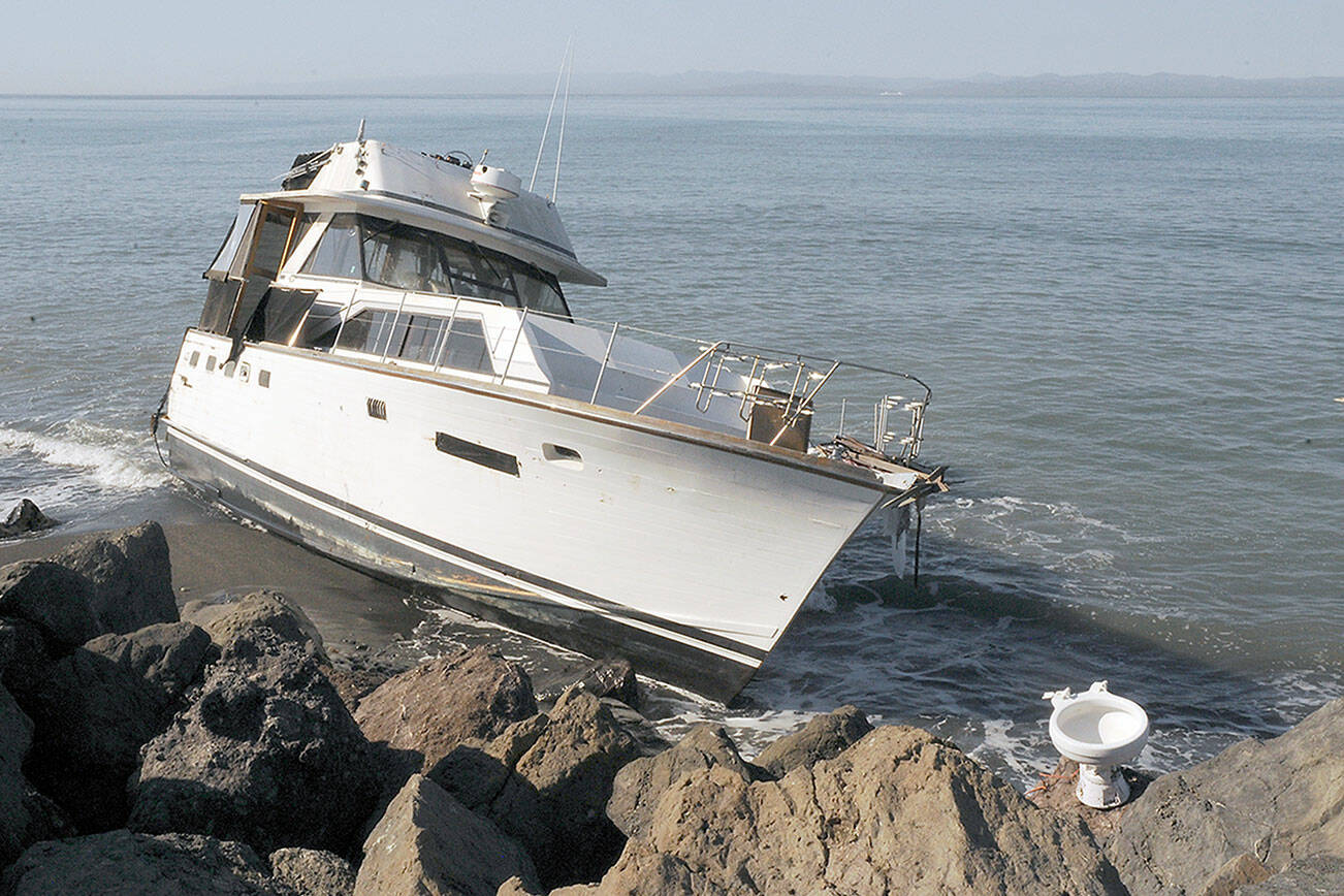 The cabin cruiser Eudora sits grounded on the north side of Ediz Hook in Port Angeles on Tuesday as a toilet, which may have been aboard the vessel, sits on the rocks above the high tide line. (Keith Thorpe/Peninsula Daily News)