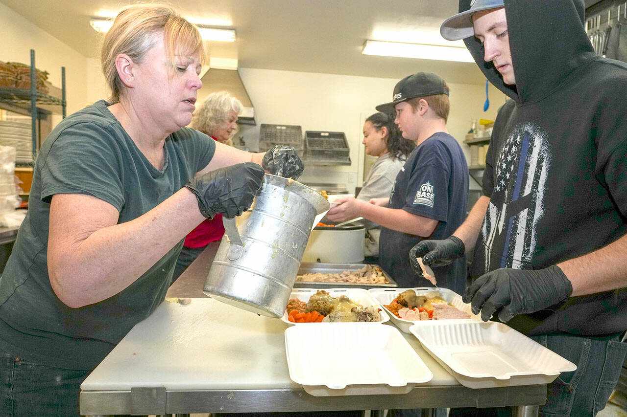 Volunteers for the Tri-Area Community Center meals program Gina Landon ladles gravy, while across from her Aiden Glenn arranges turkey slices to complete the assembly line set up to produce over 400 Thanksgiving Day turkey dinners for delivery to homeless camps and senior living facilities in Port Townsend, and as far south as Brinnon, as well as individual pick-up by those who reserved a dinner. Additional volunteers working in the background on Thursday are Melissa Layer, Rosemary Schmucker and Sean Jones. (Steve Mullensky/for Peninsula Daily News)