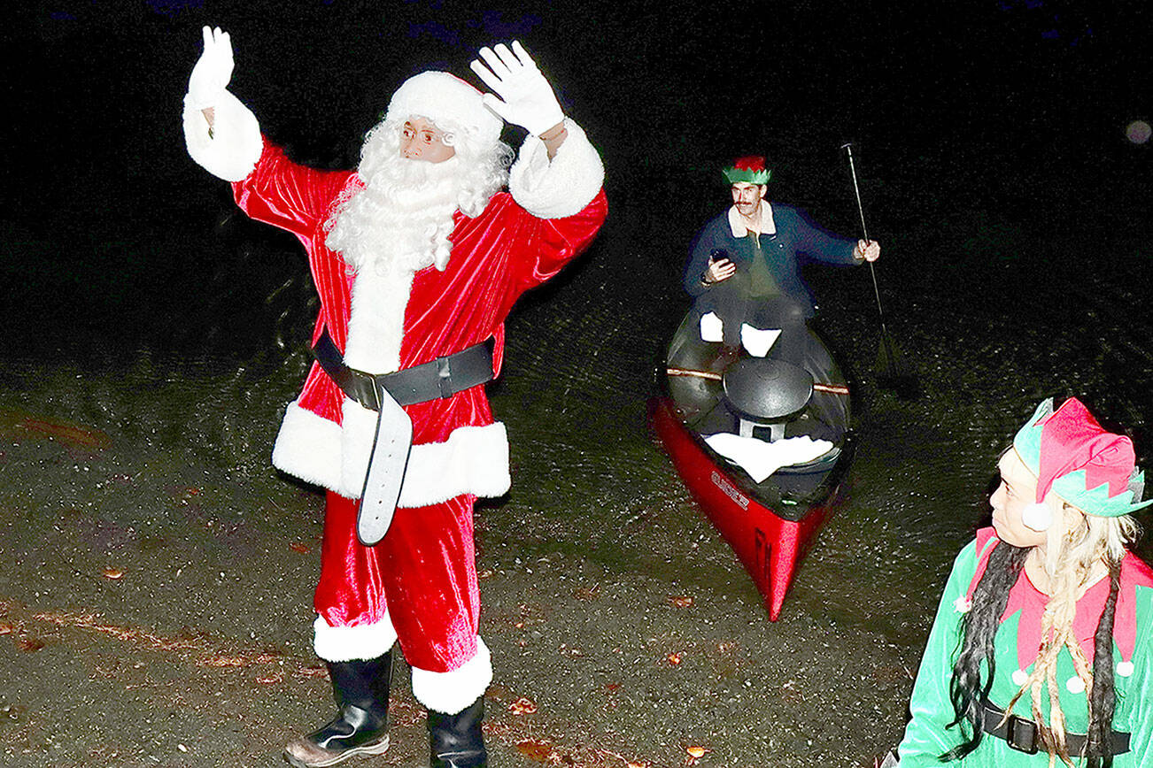 Dave Logan/for Peninsula Daily News 

Santa, played by Beau Gibson, greets the children and their parents on the shores of Lake Crescent after his arrival by canoe to the Lake Crescent Lodge on Saturday. In the canoe is his paddler Cody Fisher and the elf on the shore is Vera Tambunan. The historic lodge on Barnes Point at Lake Crescent kicked off the season with holiday lights Saturday evening.