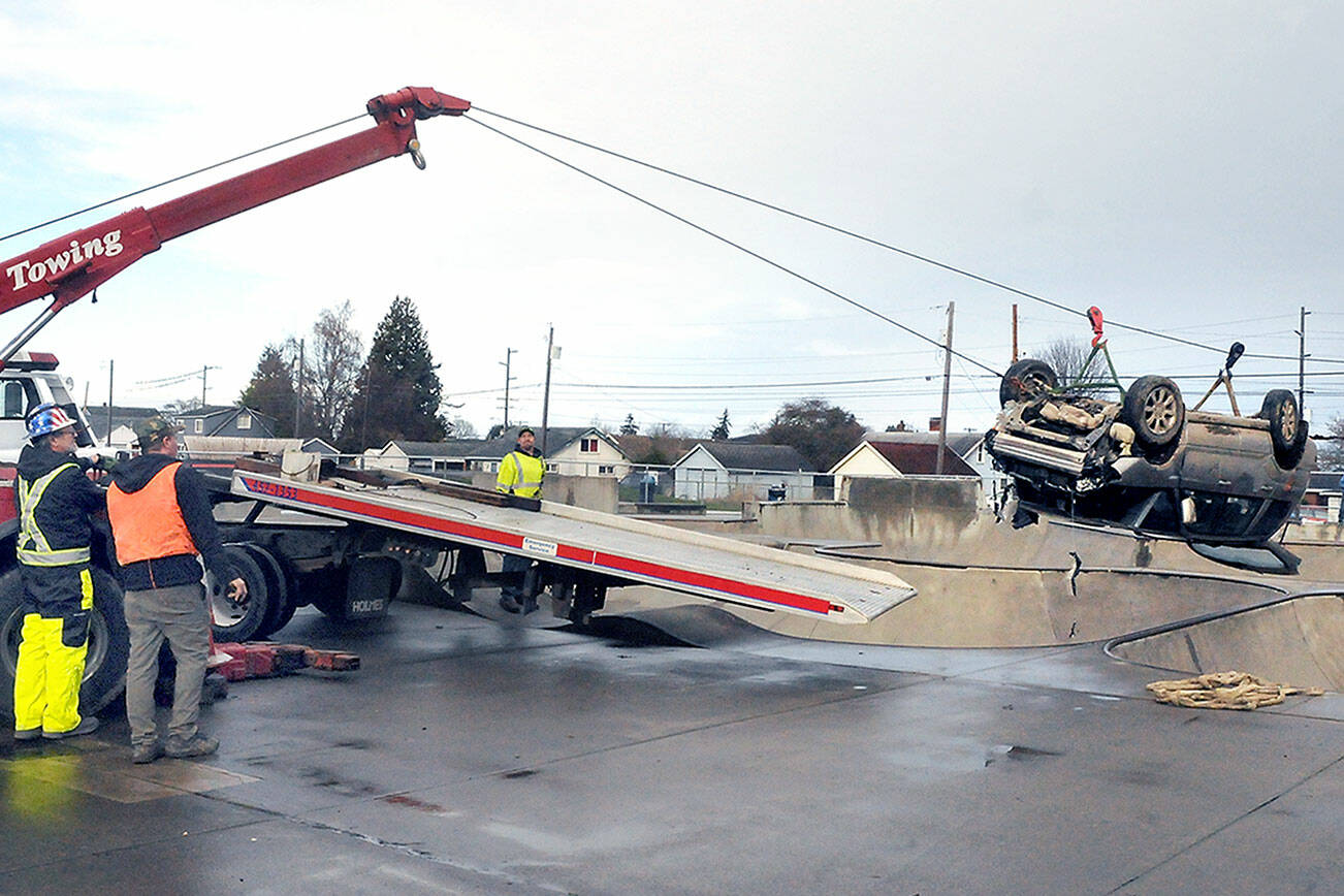 Tow truck crews hoist a car into the air and pull it to a waiting flatbed truck on Wednesday after its driver lost control and landed upside down in a skating bowl at the Port Angeles Skate Park at Erickson Playfield on Tuesday night. (Keith Thorpe/Peninsula Daily News)