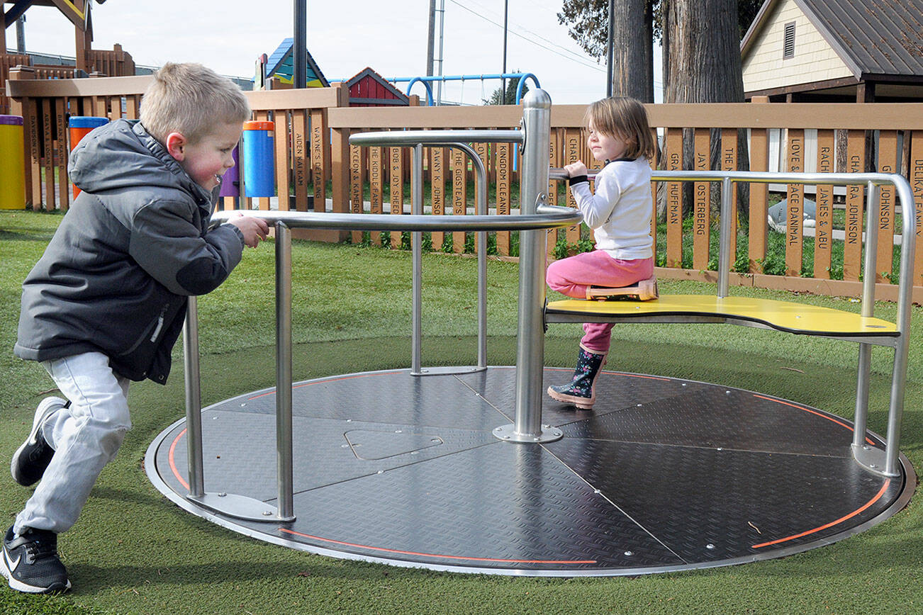 Braxton Stewart, 3, of Mill Creek pushes a merry-go-round as Kiara Ann, 4 of Sequim gets a free ride on Wednesday at the Dream Playground at Erickson Playfield in Port Angeles. The pair were enjoying a cool but clear late-winter day on the North Olympic Peninsula. (Keith Thorpe/Peninsula Daily News)