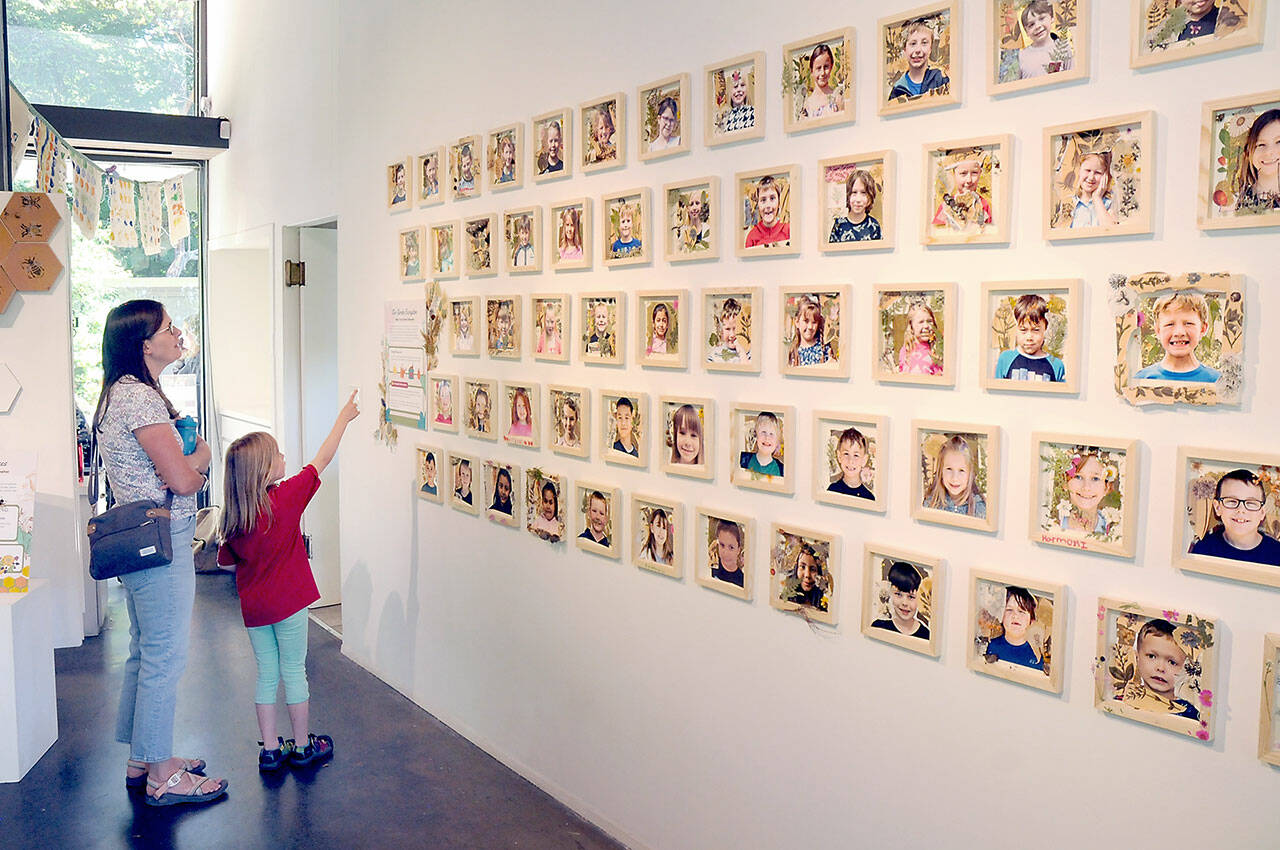 Janel Bistrika of Port Angeles and her daughter, Amelia Bistrika, 7, look at a wall of photographs of first-grade students, including Amelia, who took part in the garden-themed “Blooming Artists” exhibition during an opening reception on Tuesday at the Port Angeles Fine Arts Center. (KEITH THORPE/PENINSULA DAILY NEWS)