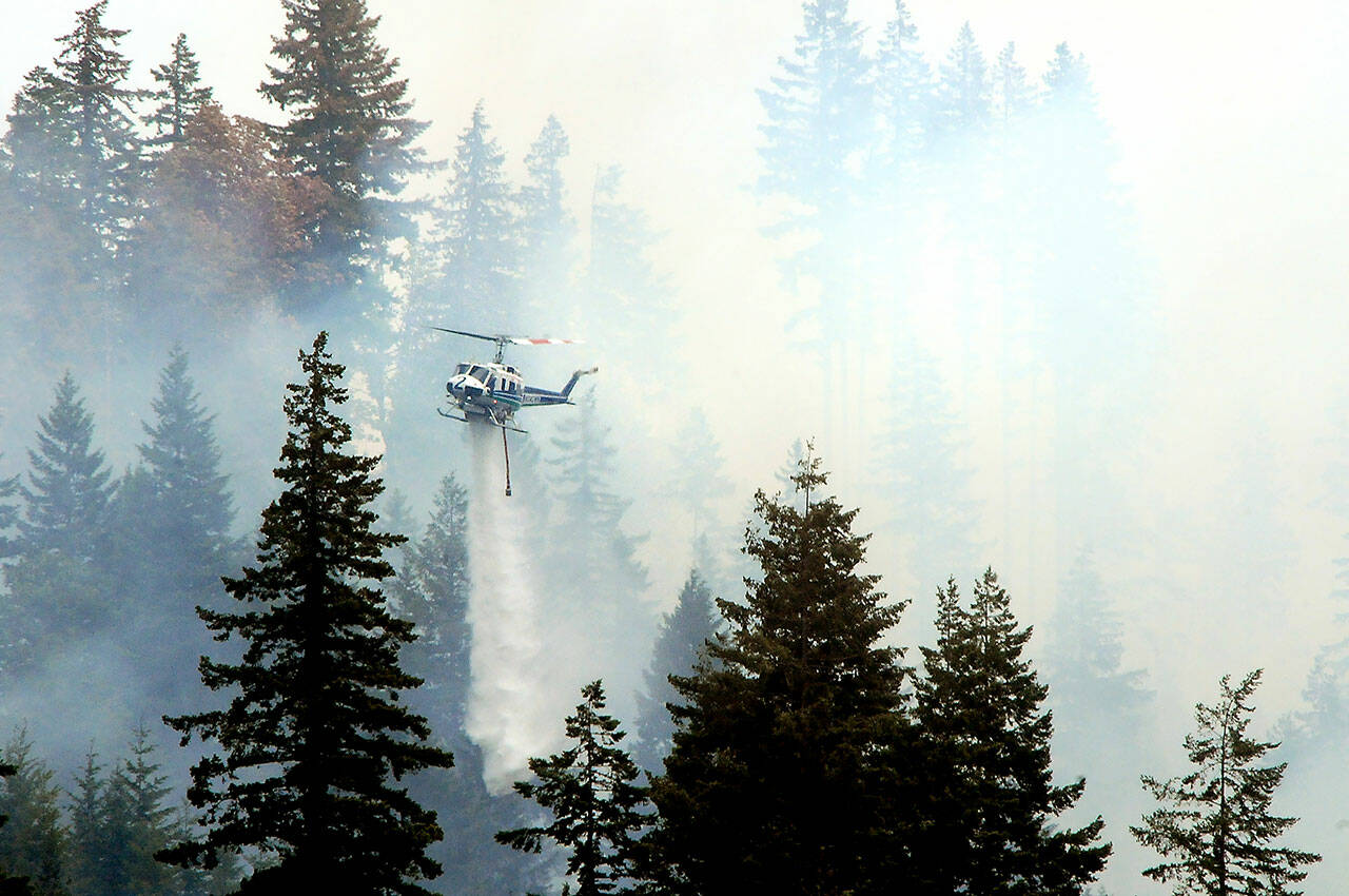 A state Department of Natural Resources helicopter flies through clouds of smoke to dump water on a hotspot of a wildland fire in the Indian Creek Valley on Sunday southwest of Port Angeles. (Keith Thorpe/Peninsula Daily News)