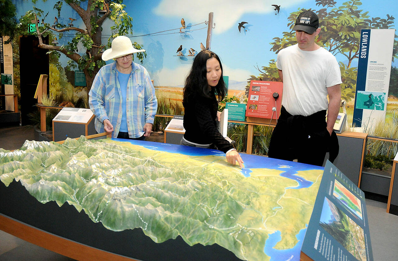 Dungeness River Nature Center visitors, from left, Chris McDonald of Port Angeles, Tram Pham of Huntington Beach, Calif., and Paul McDonald of Redmond examine a relief map display of the Dungeness River Watershed on Wednesday in Sequim. (KEITH THORPE/PENINSULA DAILY NEWS)