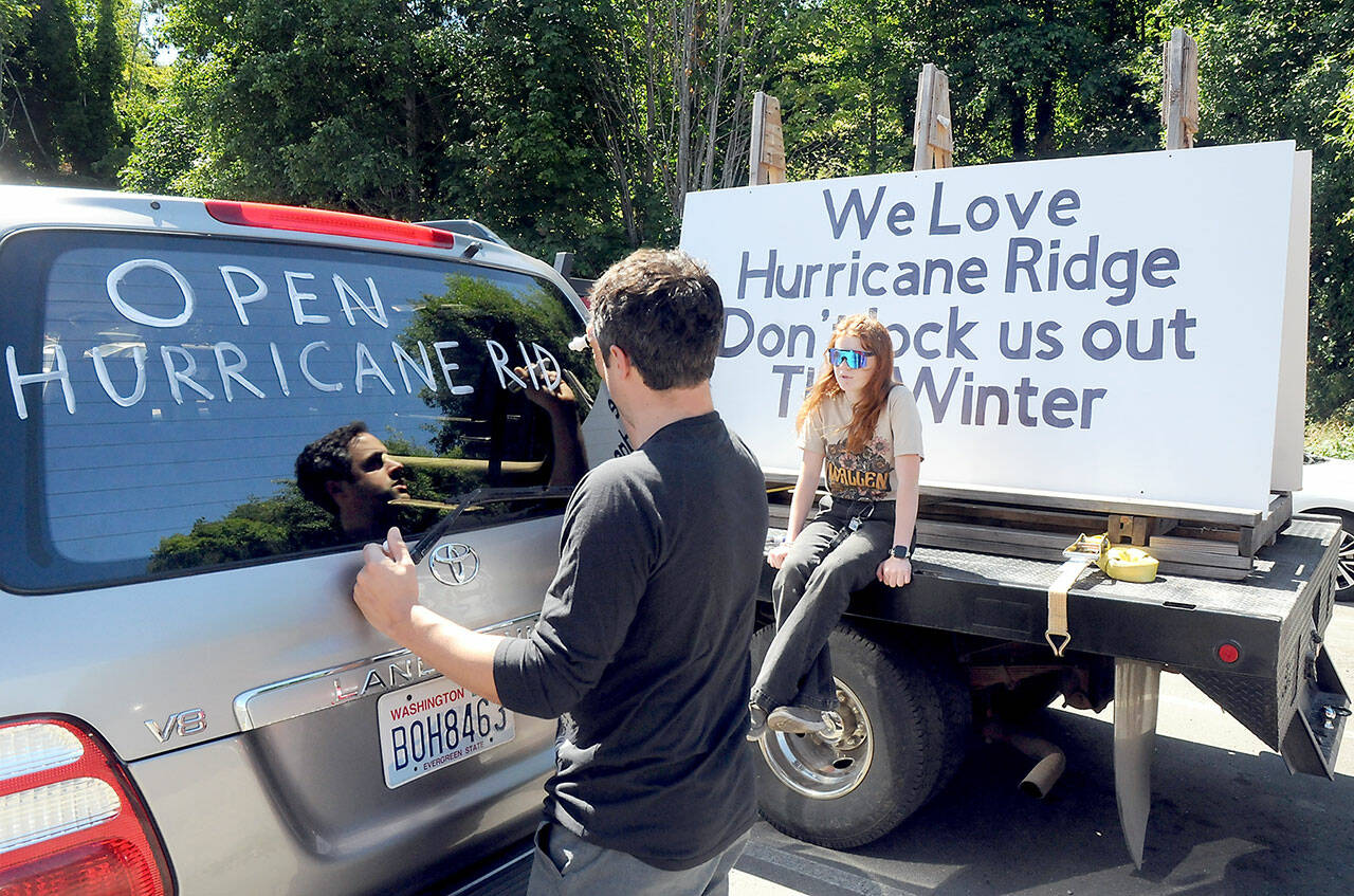 Phil Gilles of Port Angeles adds a message to keep Hurricane Ridge open during the winter ski season before taking part in a parade on Saturday co-organized by Remi Lamarshe, 13, of Port Angeles, sitting on the back of a nearby parade participant. (Keith Thorpe/Peninsula Daily News)