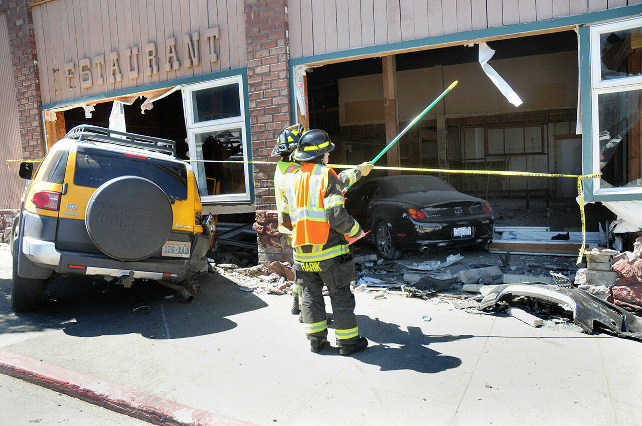 Port Angeles firefighters Ben Clark and Samantha Harik examine a gaping hole in the side of the former Delaney’s Restaurant and Bar at Front and Lincoln streets in downtown Port Angeles after a three-vehicle collision sent two vehicles into the building on Wednesday. (Keith Thorpe/Peninsula Daily News)