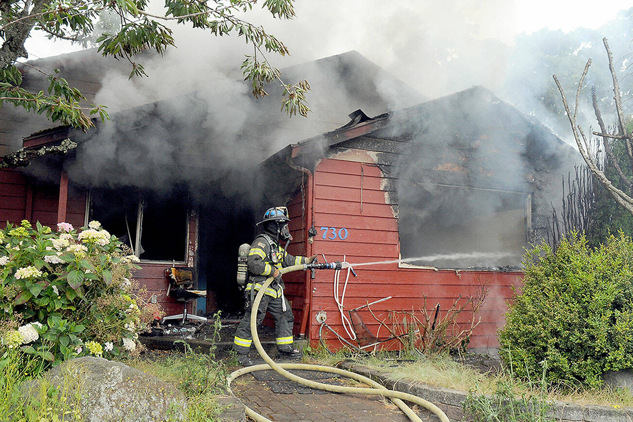 Port Angeles firefighter Paul Johnston sprays water onto a burning house at 730 E. Fourth St. on Saturday morning. (Keith Thorpe/Peninsula Daily News)