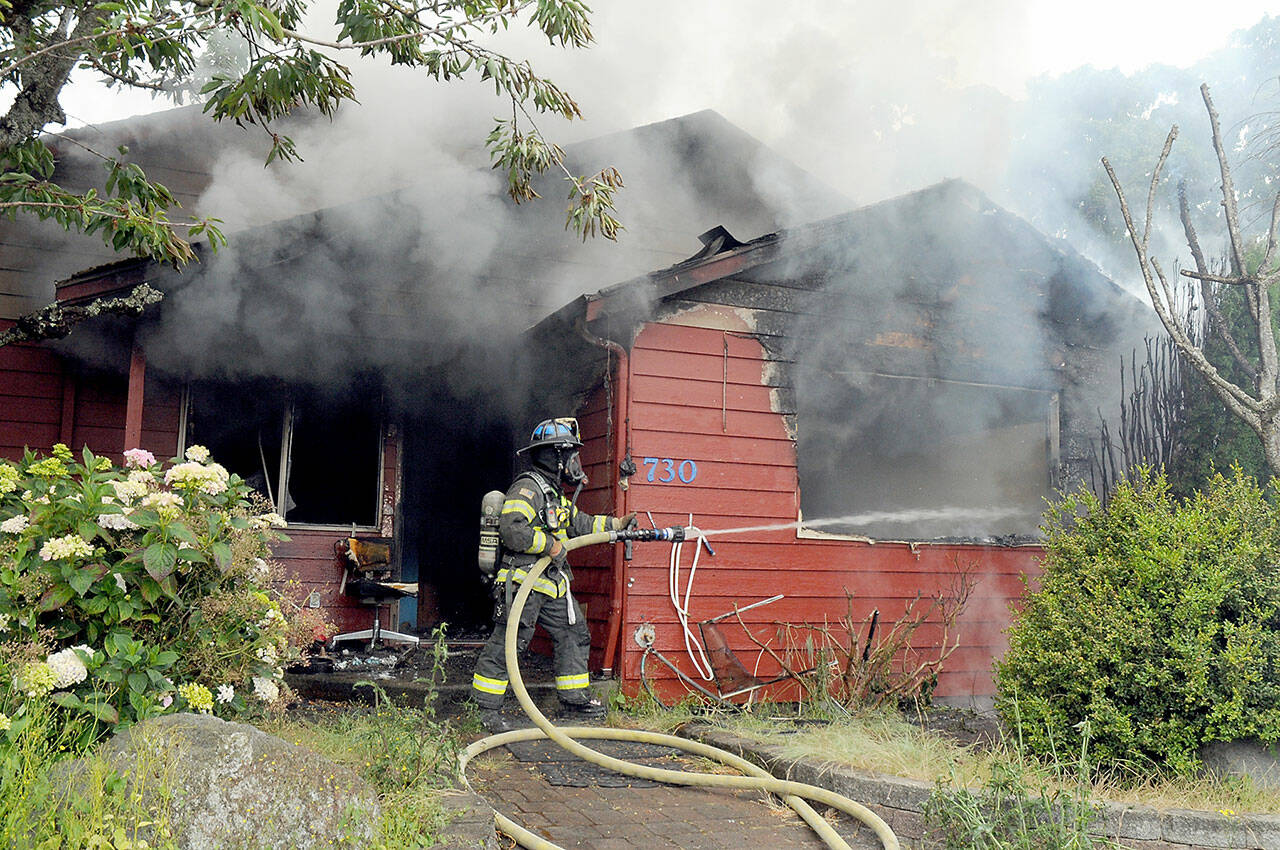 Port Angeles firefighter Paul Johnston sprays water onto a burning house at 730 E. Fourth St. on Saturday morning. (Keith Thorpe/Peninsula Daily News)