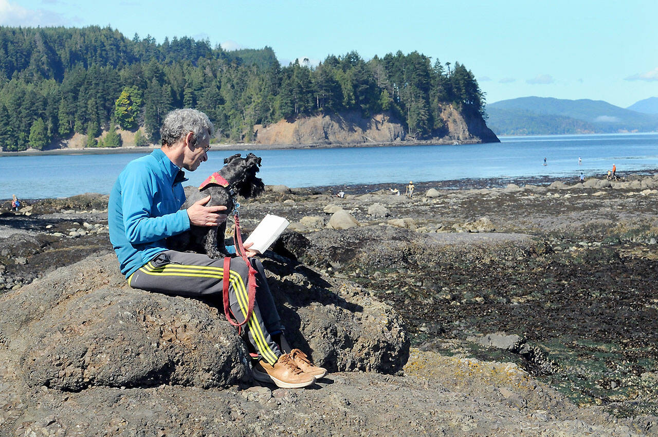 Mike Nossal of Seattle, along with his dog Pico, reads a book on a rocky outcrop overlooking Tongue Point at the Salt Creek Recreation Area on Thursday north of Joyce. (KEITH THORPE/PENINSULA DAILY NEWS)