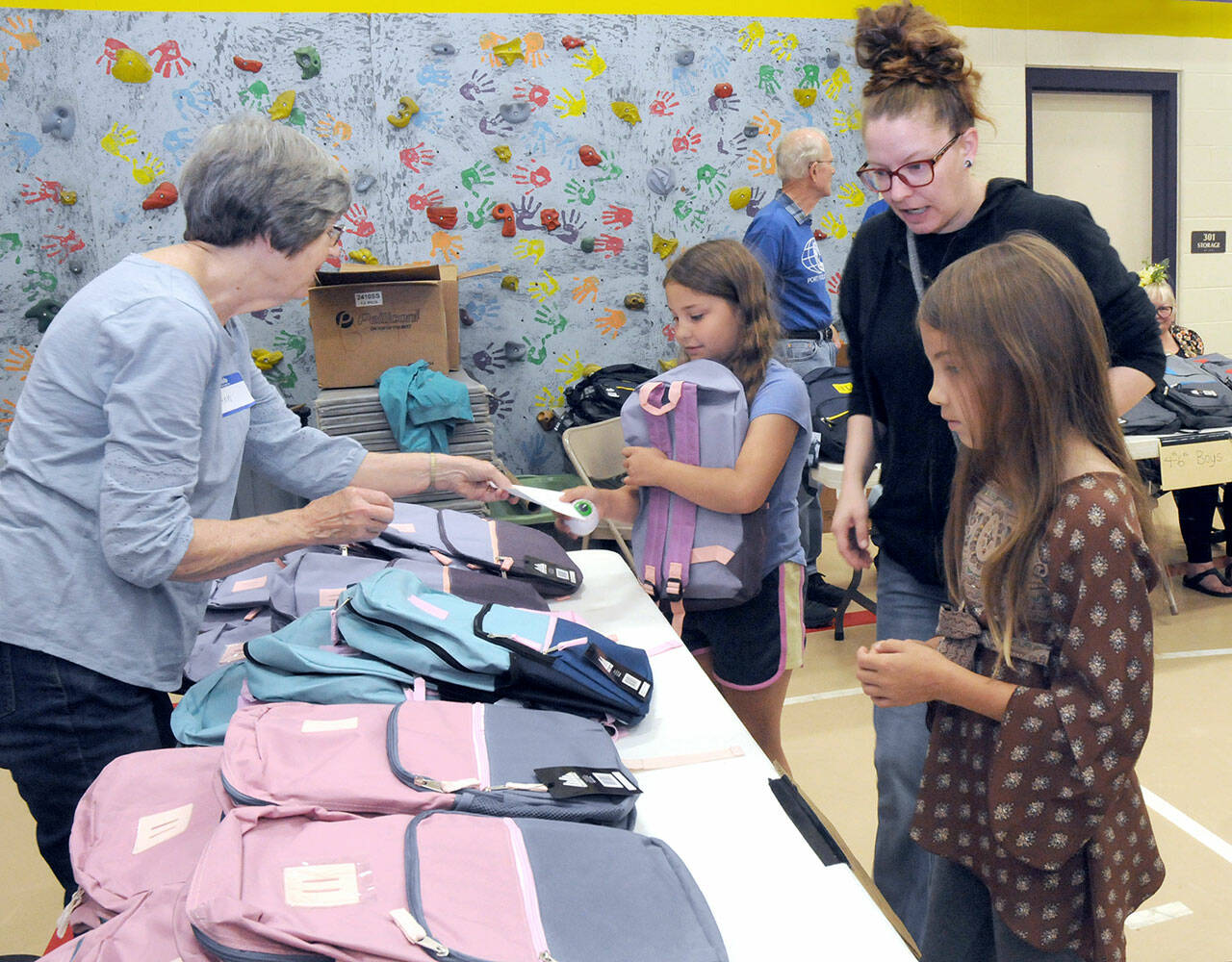 Julia Smith of Port Angeles, center right, oversees her children, fourth-grader Julia Smith, 9, and fifth-grader Shelby Smith, 10, right, pick out backpacks filled with school supplies as volunteer Ann West assists with distribution during Saturday’s back-to-school fair at Jefferson Elementary School in Port Angeles. During the event, students were given free school supplies, with family service opportunities, as well as a lunch, made available at the approach of the 2023-24 school year. (Keith Thorpe/Peninsula Daily News)