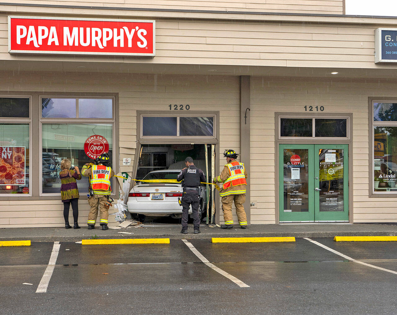 Personnel from East Jefferson Fire and Rescue (EJFR) and Port Townsend police investigate the scene where a Toyota driven by a Quilcene woman crashed into the doorway of Papa Murphy’s pizza shop at 1220 W. Sims Way in Port Townsend before noon on Tuesday. She was not injured, but she was shaken up by the incident that occurred when her foot slipped off the brake pedal and hit the accelerator, according to EJFR Chief Bret Black. (Steve Mullensky/for Peninsula Daily News)