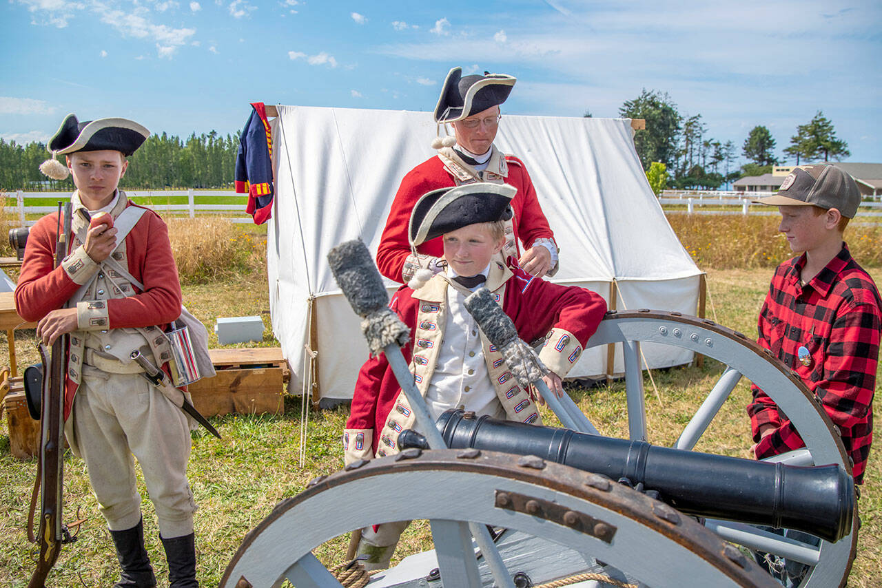 Dressed as British soldiers at the time of the American Revolution, Peter Berneking of Sequim, Thomas House-Higgins of Olympia and Luke Berneking explain about how a three pound ball fits into this particular cannon while Caleb Berneking looks on during the 2022 event.