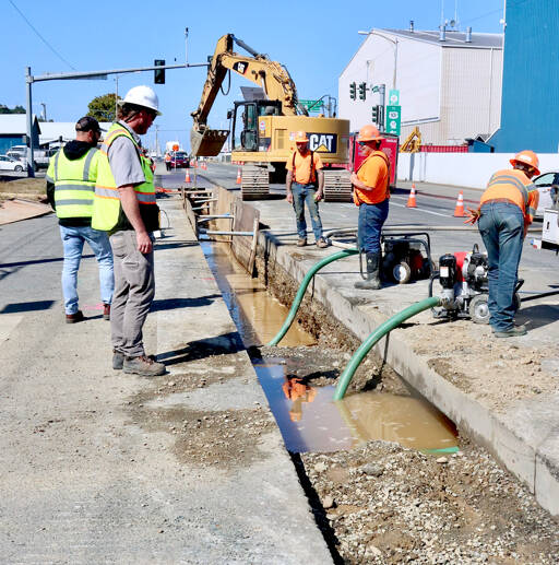 Weston Jorgensen, capital projects inspector, at left, watches as workers dewater a trench for a sewer main installation on Marine Drive at Tumwater Truck Route in Port Angeles after a water main was damaged Thursday morning. Work on the sewer main crossing at Tumwater Truck Route was expected to be finished on Thursday, but the water main damage slowed that work, according to city civil engineer Lucio Baack. He anticipated the Tumwater Truck Route traffic signal to be shut off temporarily today while the water main is repaired. The work is part of a larger project to install a new sewer force main for Pump Station 3. (Dave Logan/for Peninsula Daily News)