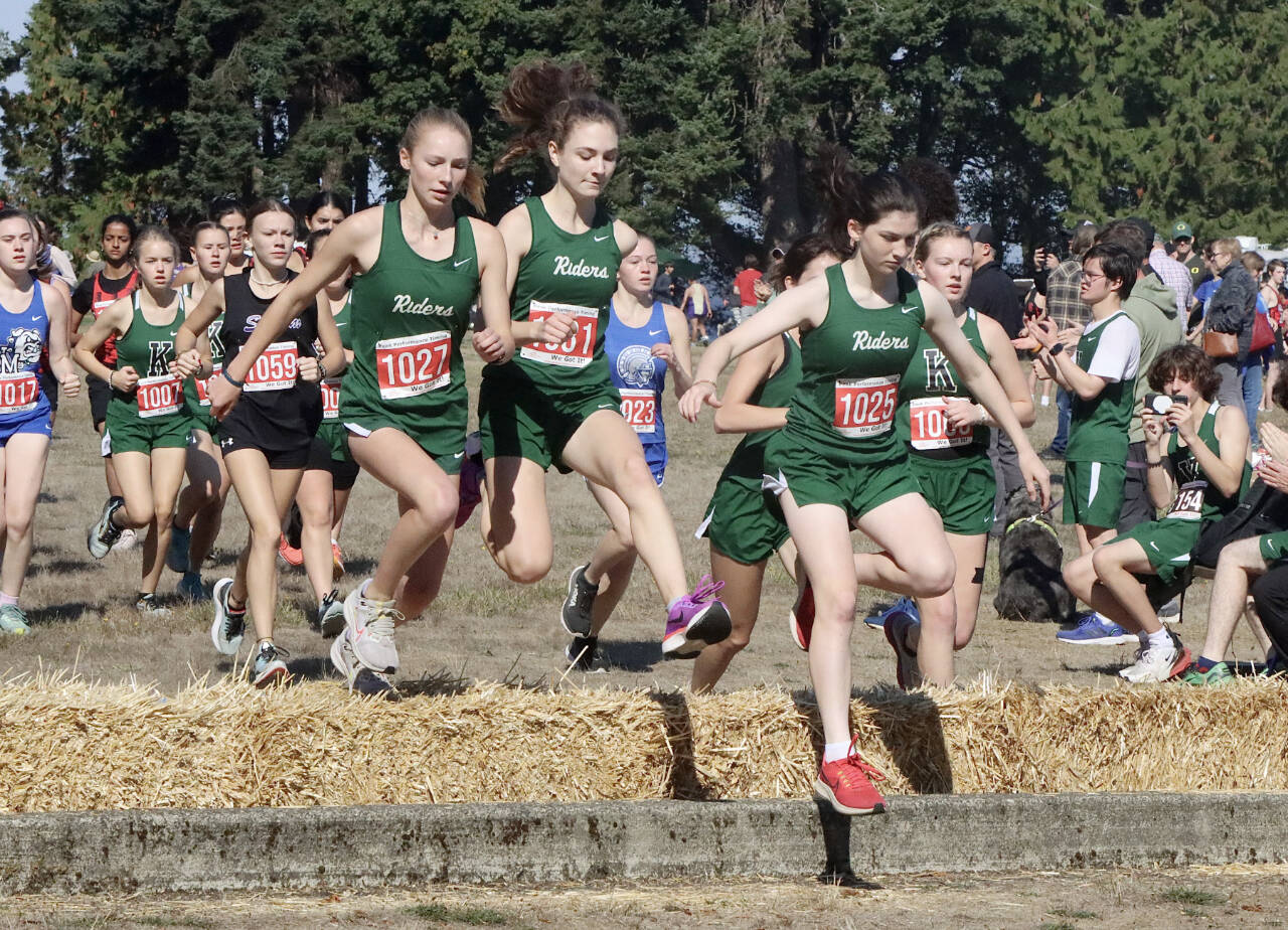 Port Angeles’ Leia Larson, Faerin Tate and Miriam Cobb jump over the hay bales at the start of the 45th annual Salt Creek Invitational at Salt Creek County Park on Saturday. Larson and Cobb both finished in the to 10 while all three Roughriders finished in the top 20. (Dave Logan/for Peninsula Daily News)