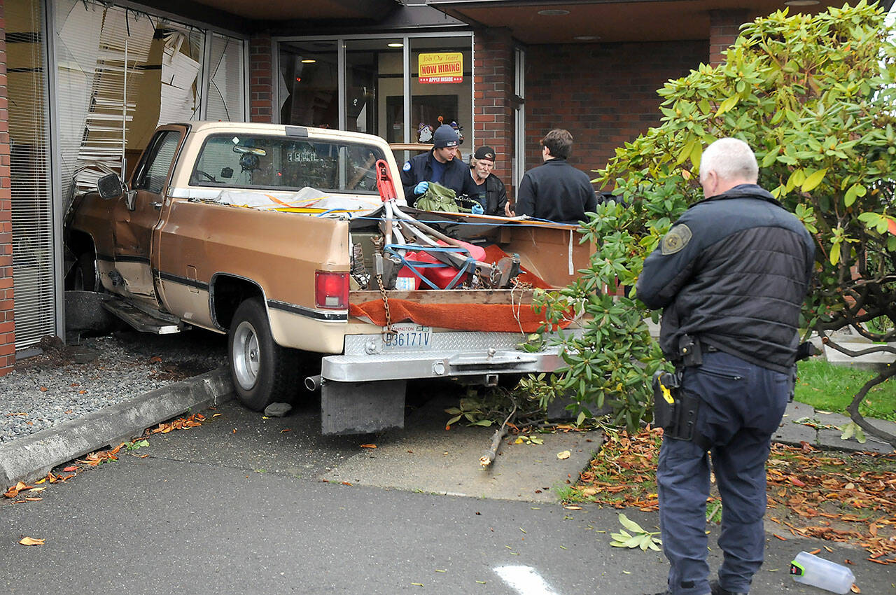 A two-vehicle wreck ended in a pickup driving into Caregivers Home Health at 622 E. Front St. early Tuesday afternoon, according to Port Angeles Police Sgt. Kevin Miller, pictured far right. The pickup, driven by Linda Turman of Port Angeles, was on the far right of the road when it switched to the left lane, which was occupied by a late model Ford Mustang, Miller said. The pickup hit the building. Turman was reported in satisfactory condition at Olympic Medical Center later in the day. The Mustang was damaged but did not crash into anything or block traffic. Turman was cited for improper lane use, Miller said. (Keith Thorpe/Peninsula Daily News)