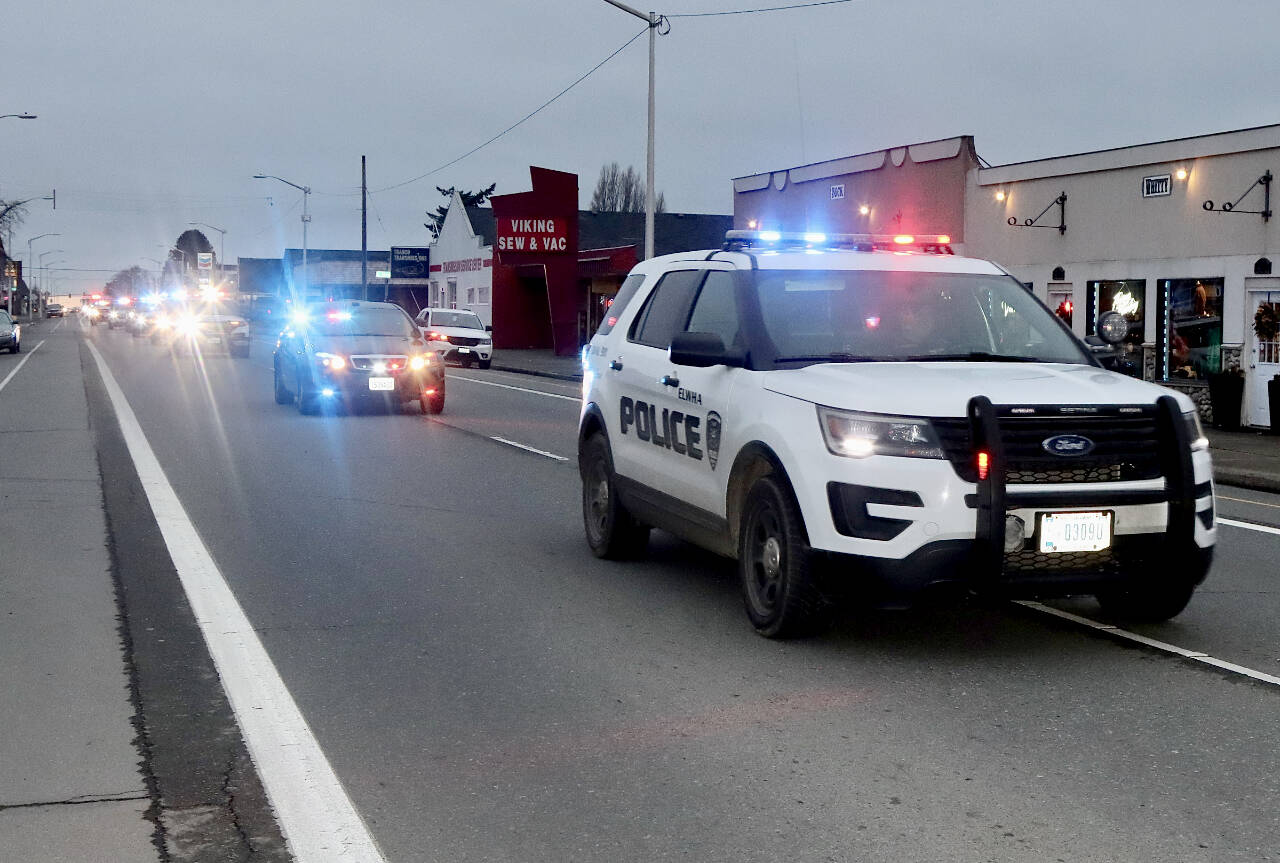 A parade honoring Ron Cameron, with nearly two dozen vehicles with lights flashing, heads east on First Street in Port Angeles. (DAVE LOGAN/FOR PENINSULA DAILY NEWS )