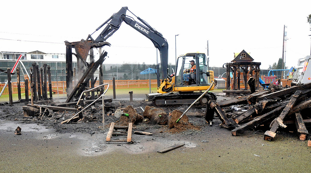 An excavator operated by Jad Groves of the Port Angeles Public Works Department removes the charred remains of the treehouse structure at the Dream Playground at Erickson Playfield on Thursday after much of the playground was destroyed by fire early Wednesday morning. (Keith Thorpe/Peninsula Daily News)