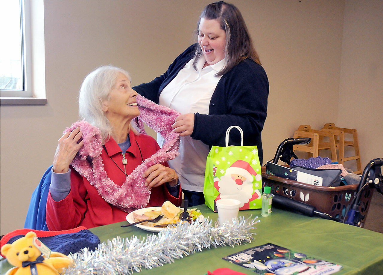 Marilyn Van Patter of Port Angeles, seated, is complimented on her decorative scarf by Capt. Crystal Birks of the Salvation Army of Port Angeles during Friday’s pre-Christmas lunch at the corps facility. The meal included a clothing giveaway and gifts for participants. (KEITH THORPE/PENINSULA DAILY NEWS)