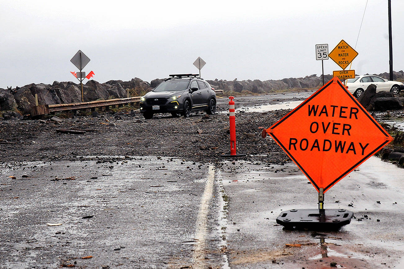 A car picks its way through a field of rocks and other debris pushed by wind-driven waves and high tides over Ediz Hook Road in Port Angeles on Tuesday. The city Public Works Department has closed the road. (Keith Thorpe/Peninsula Daily News)