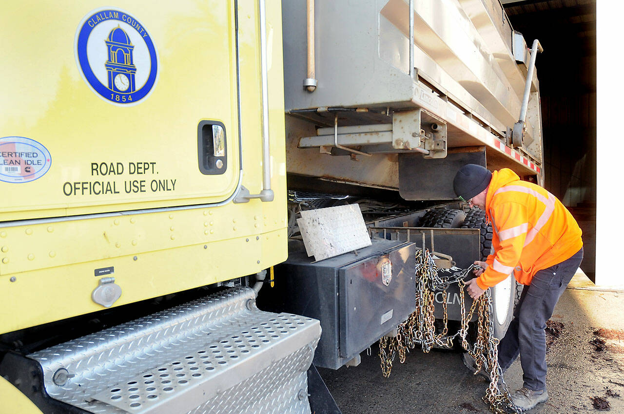 Clallam County Road Department maintenance worker Jeremy Reeves loads a set of tire chains onto a county sand truck on Wednesday at the county shop in Port Angeles in preparation for potential snow on the North Olympic Peninsula. (Keith Thorpe/Peninsula Daily News)