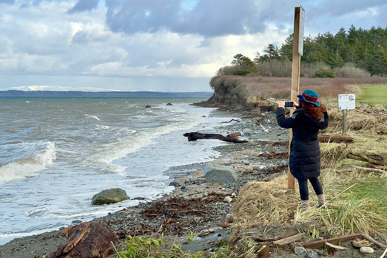 Port Townsend’s Margo Karler uses her cell phone to photograph wave action at North Beach in Port Townsend on Thursday. (Steve Mullensky/for Peninsula Daily News)