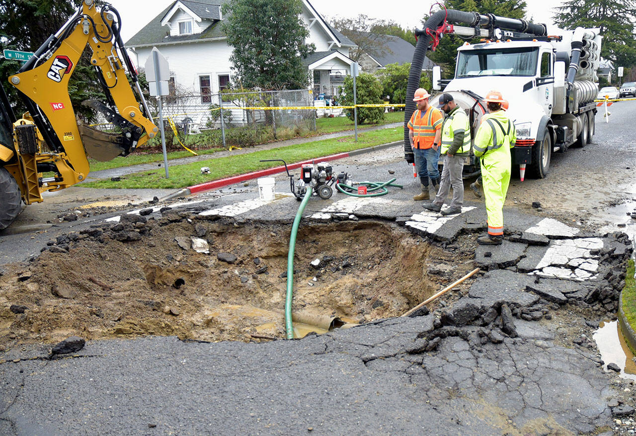 A Port Angeles Public Works crew examines the hole left at 11th and Oak streets after a water main break sent a geyser of water into the air Saturday morning, damaging the road surface. (Keith Thorpe/Peninsula Daily News)