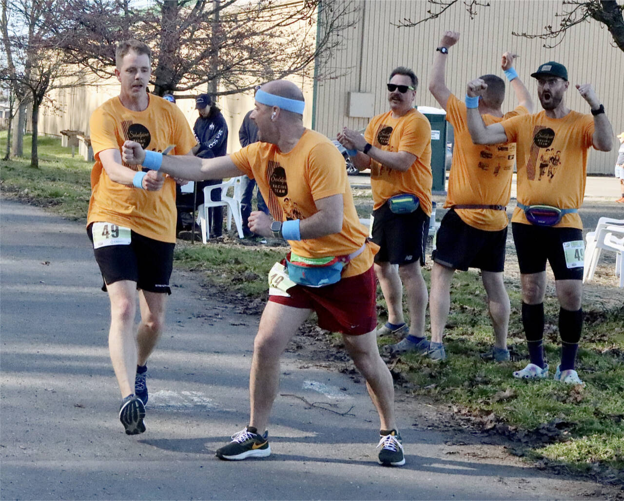 Chris Hartman of the Olympic Peninsula Frosty Moss relay team Sub Alpine Tees passes the relay stick off to teammate Chris Cummings as the rest of Sub Alpine team members cheer him on. Sub Alpine Tees was one of 61 relay teams to compete. (Dave Logan/for Peninsula Daily News)