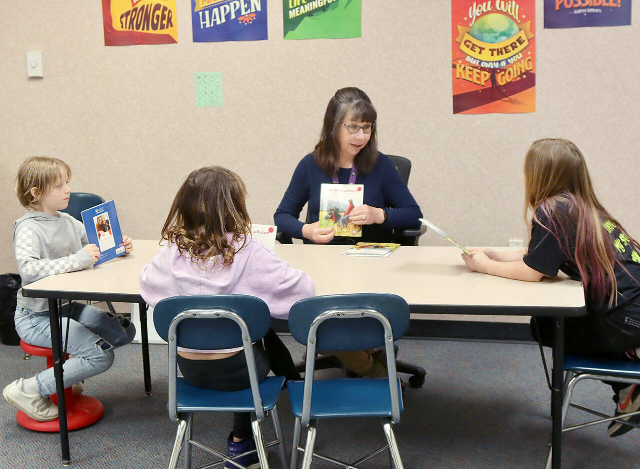 Becca Paul, a paraeducator at Jefferson Elementary in Port Angeles, helps introduce a new book for third-graders, from left, Margret Trowbridge, Taezia Hanan and Skylyn King, to practice reading in the Literacy Lab. The book is entitled “The Girl With A Vision.” (Dave Logan/for Peninsula Daily News)