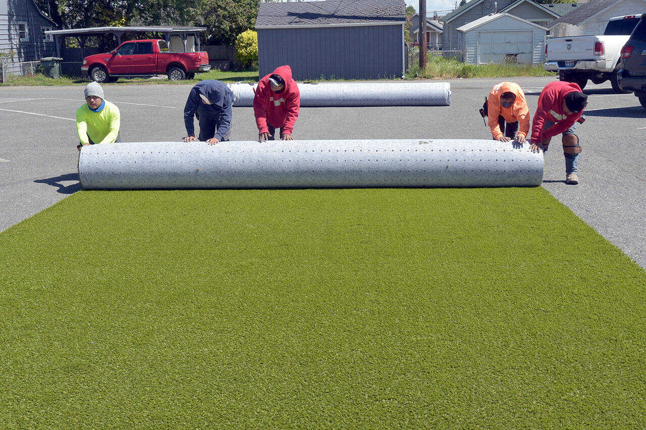A work crew from the Texas-based ForeverLawn rolls up a piece of cut playground surface in the parking lot of Erickson Playfield in preparation for installation at the nearby Dream Playground in Port Angeles. The crew was contracted to install the padded play area after a five-day community build last week to replace portions of the playground that were destroyed by arson in December. (Keith Thorpe/Peninsula Daily News)