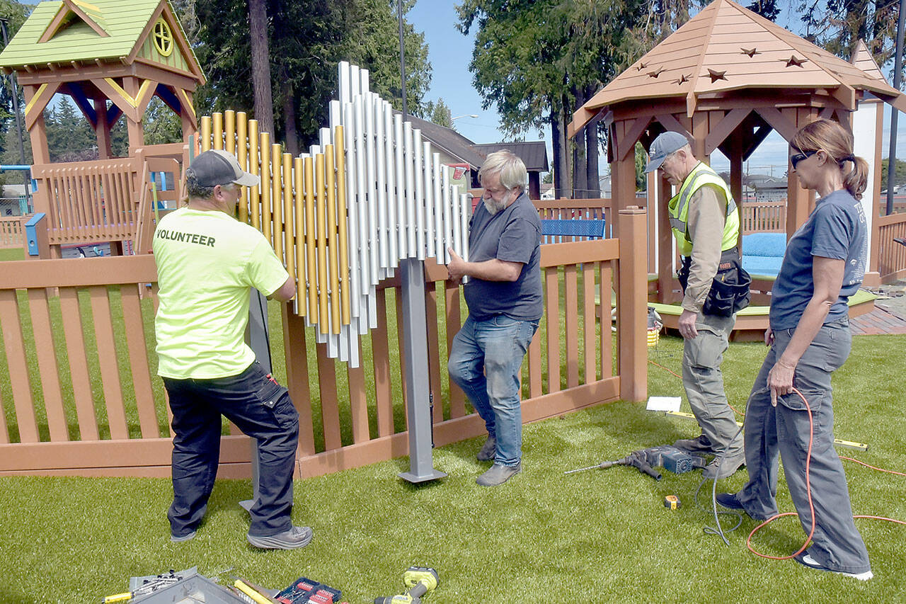 Jason Minnoch, left, and Jim deBord move a set of musical chimes as Al Oman and Jo Johnston look on during preparations on Wednesday for Sunday’s playground opening of the Dream Playground at Erickson Playfield in Port Angeles. The playground, rebuilt by volunteers in May after much of it was destroyed by arson in December, will host an official reopening and dedication ceremony at 3 p.m. Sunday. (Keith Thorpe/Peninsula Daily News)