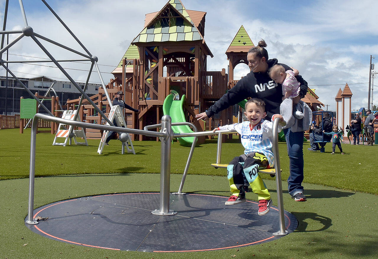 Three-year-old Archie Hanson takes a spin on a merry-go-round pushed by his mother, Justine Hanson of Port Angeles, with sister Arlene Hanson 7 months, during Sunday’s grand reopening of the Dream Playground at Erickson Playfield in Port Angeles. The playground was rebuilt earlier this month by volunteers after an arson fire destroyed much of the playground equipment in December. Although there are still details to attend to and minor adjustments to be made, the facility will be open daily from dawn until dusk. (KEITH THORPE/PENINSULA DAILY NEWS)