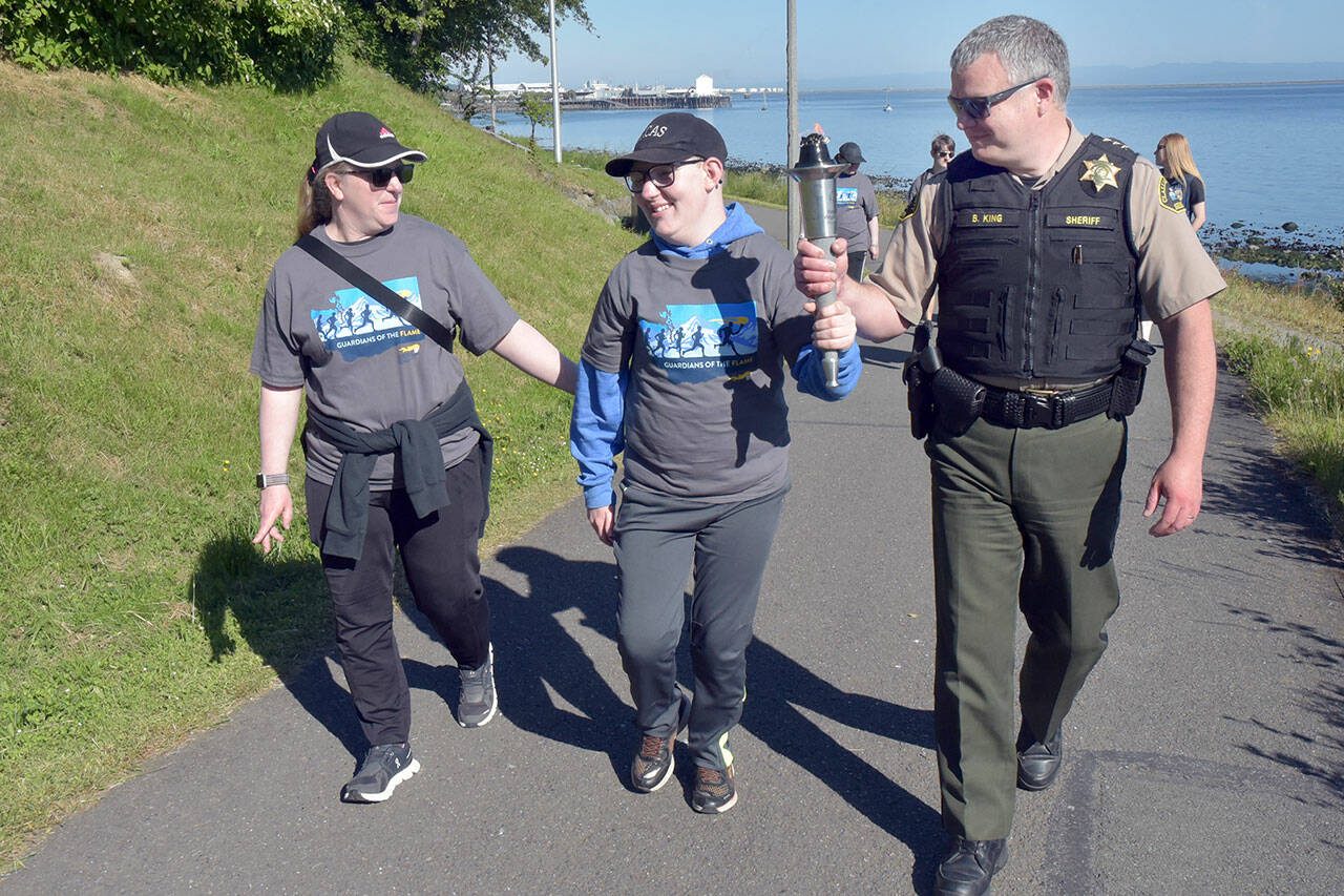 Clallam County Sheriff Brian King, right, carries a ceremonial torch with Special Olympian William Sirguy, center, accompanied by his mother, Katie Sirguy, during Friday’s Special Olympics Law Enforcement Torch Run along the Waterfront Trail in Port Angeles. The event, designed to raise awareness and funds for the Special Olympics movement, brought together law enforcement officers from Clallam, Jefferson and Kitsap counties for a march across the North Olympic Peninsula. (Keith Thorpe/Peninsula Daily News)