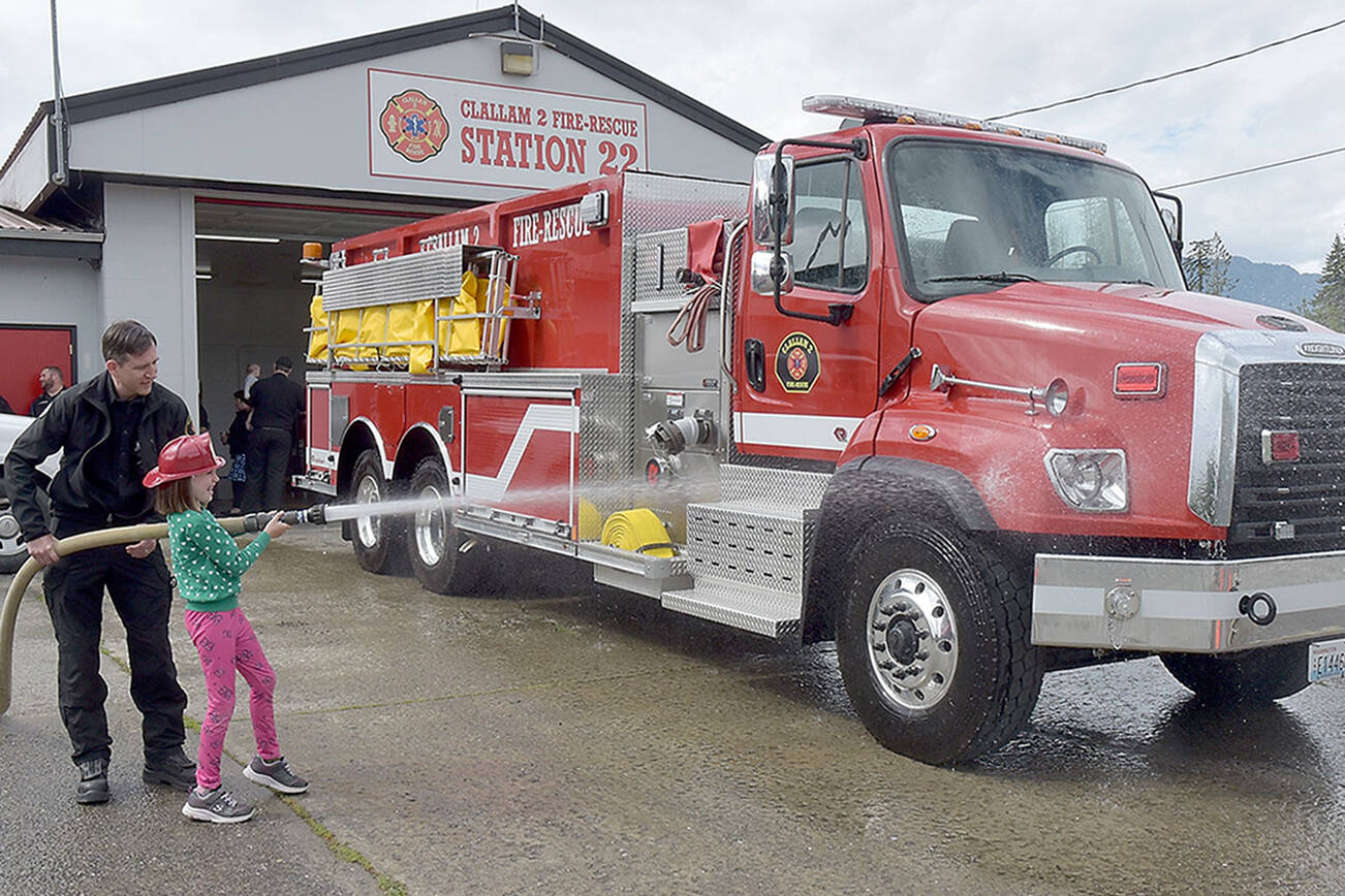 Abby Counts, 8, with assistance from her father, Taylor Counts, an EMT with Clallam 2 Fire-Rescue, gives a newly acquired tender truck a ceremonial wash down during a push-in ceremony on Saturday at the district’s Station 22. The truck, tender 22, cost $459,439 and was paid for by the fire district’s 2020 levy lid lift. Saturday’s ceremony also included a blessing by the Lower Elwha Klallam Tribe and a “push-in” of the truck into its berth. The tender replaces a 31-year-old truck that had reached the end of its useful life. (Keith Thorpe/Peninsula Daily News)