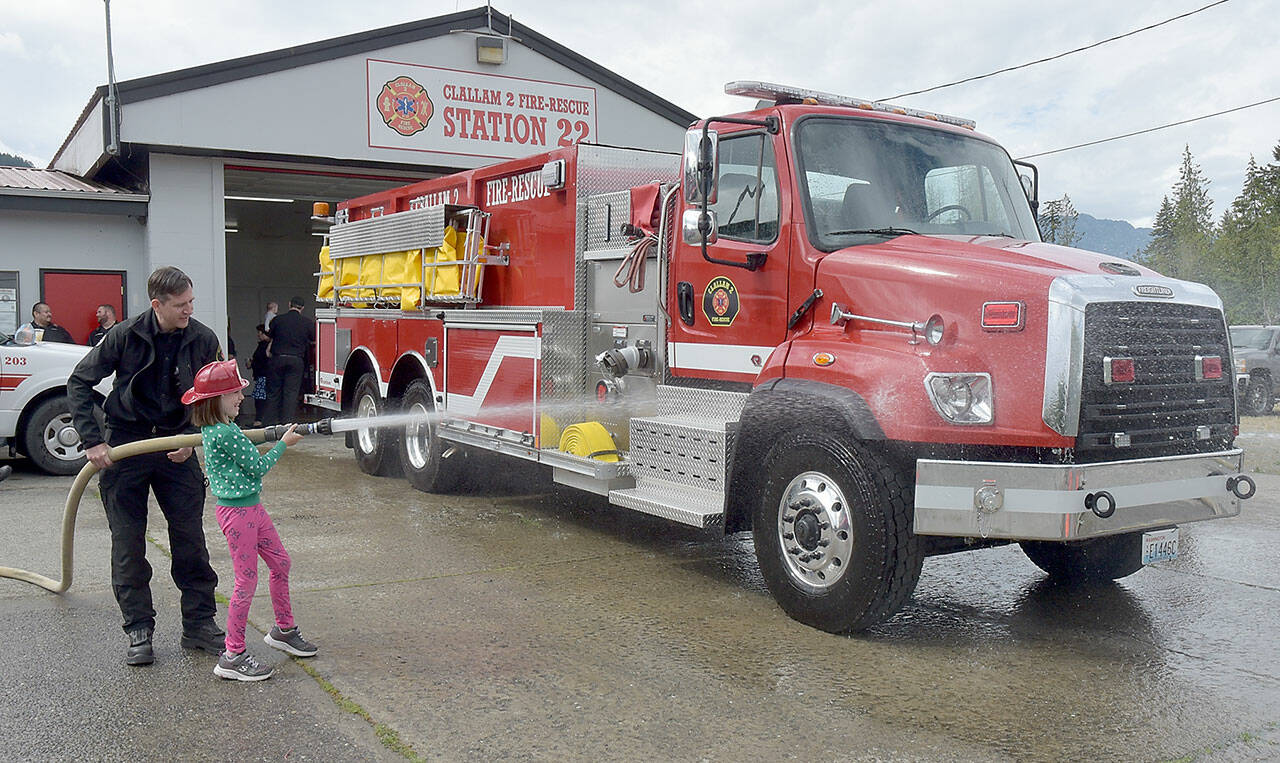 Abby Counts, 8, with assistance from her father, Taylor Counts, an EMT with Clallam 2 Fire-Rescue, gives a newly acquired tender truck a ceremonial wash down during a push-in ceremony on Saturday at the district’s Station 22. The truck, tender 22, cost $459,439 and was paid for by the fire district’s 2020 levy lid lift. Saturday’s ceremony also included a blessing by the Lower Elwha Klallam Tribe and a “push-in” of the truck into its berth. The tender replaces a 31-year-old truck that had reached the end of its useful life. (Keith Thorpe/Peninsula Daily News)