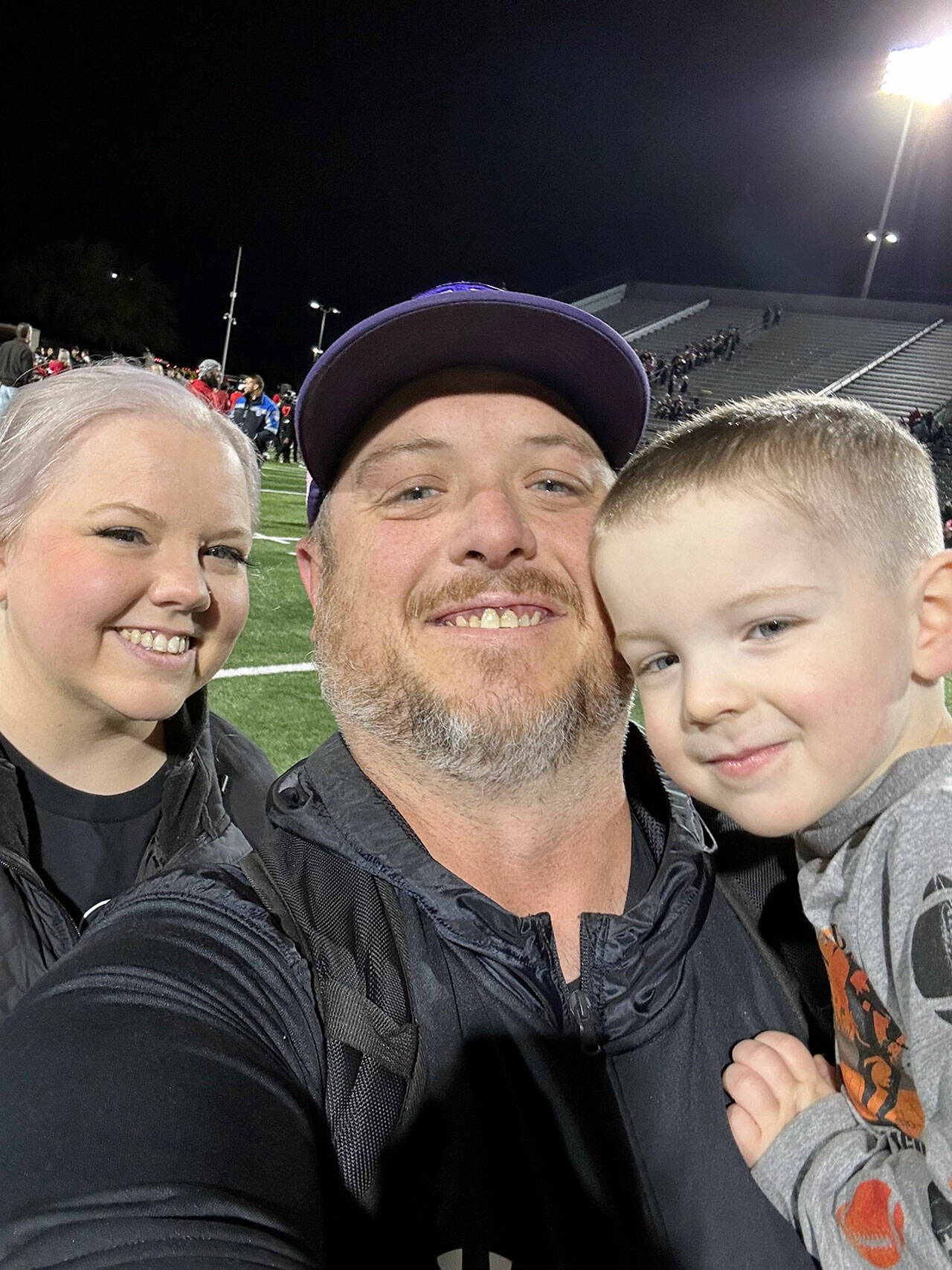 New Sequim athletic director/head football coach Ian Henley takes a family photo with his wife Jessica and son Rhys after a football game.