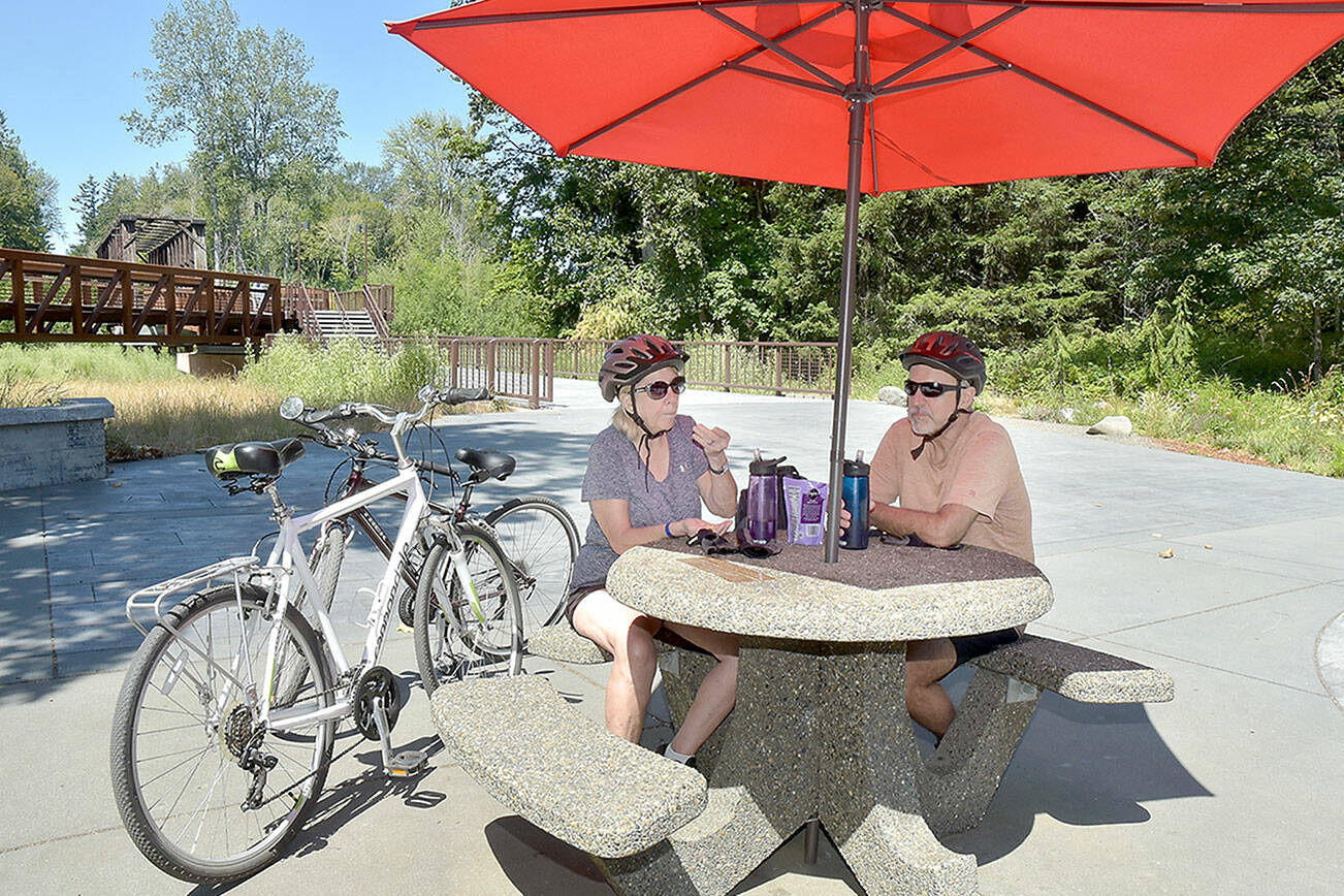 Twyla and Doug Falsteisek, who split their time between Port Angeles and Sun City West, Ariz., take a break from their bike ride on the patio of the Dungeness River Nature Center along the Dungeness River in Sequim on Wednesday. The couple took advantage of summer weather for an excursion on the Olympic Discovery Trail. (Keith Thorpe/Peninsula Daily News)