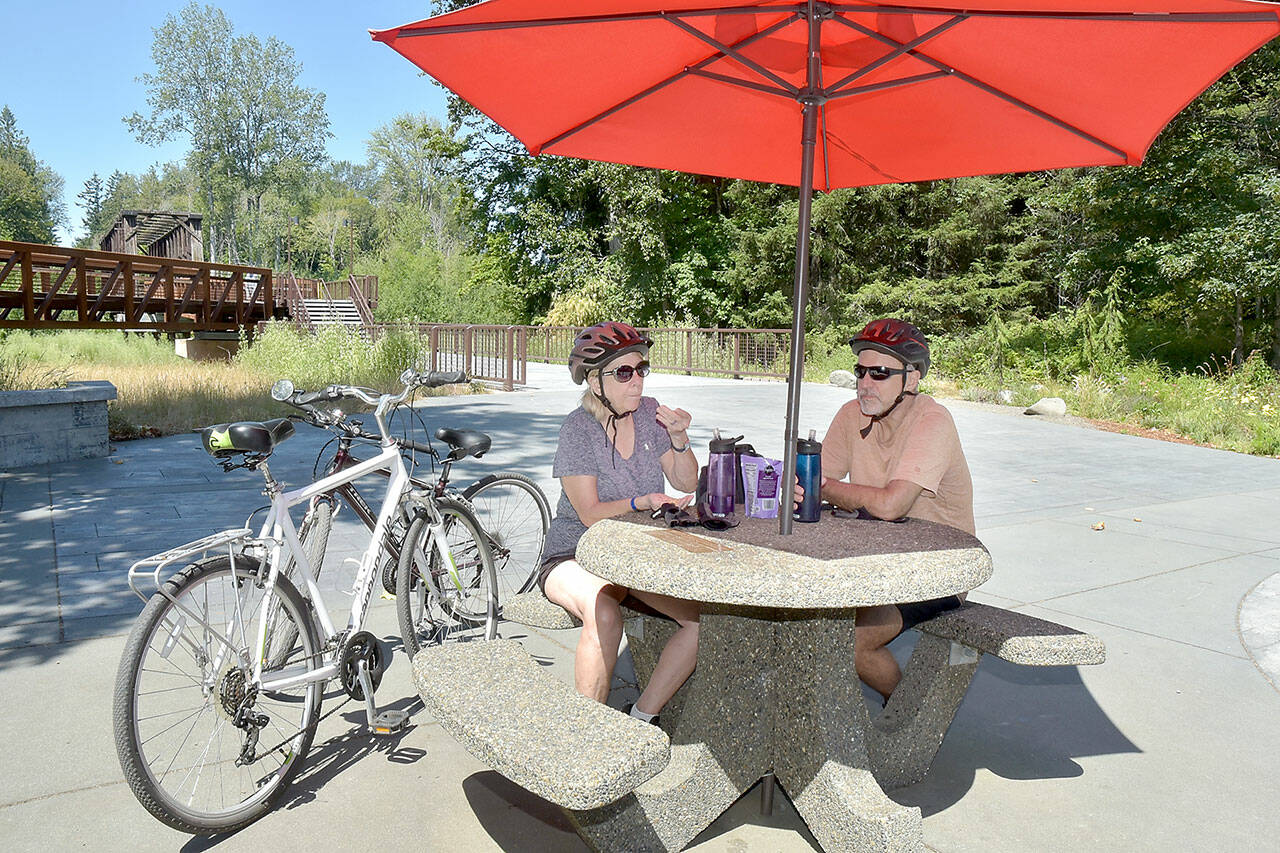 Twyla and Doug Falsteisek, who split their time between Port Angeles and Sun City West, Ariz., take a break from their bike ride on the patio of the Dungeness River Nature Center along the Dungeness River in Sequim on Wednesday. The couple took advantage of summer weather for an excursion on the Olympic Discovery Trail. (Keith Thorpe/Peninsula Daily News)