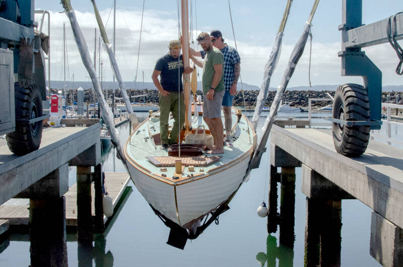 From left, Leland Gibson, Tucker Piontek and Jeff Matthews are lowered into the water aboard Fern, a Nordic folk boat commissioned by Michigan resident Charles Jahn, who was present to see his boat in the water for the first time on Friday at Port Townsend’s Boat Haven Marina. Fern was built over three years by three separate classes of students at The Northwest School of Wooden Boatbuilding. (Elijah Sussman/Peninsula Daily News)