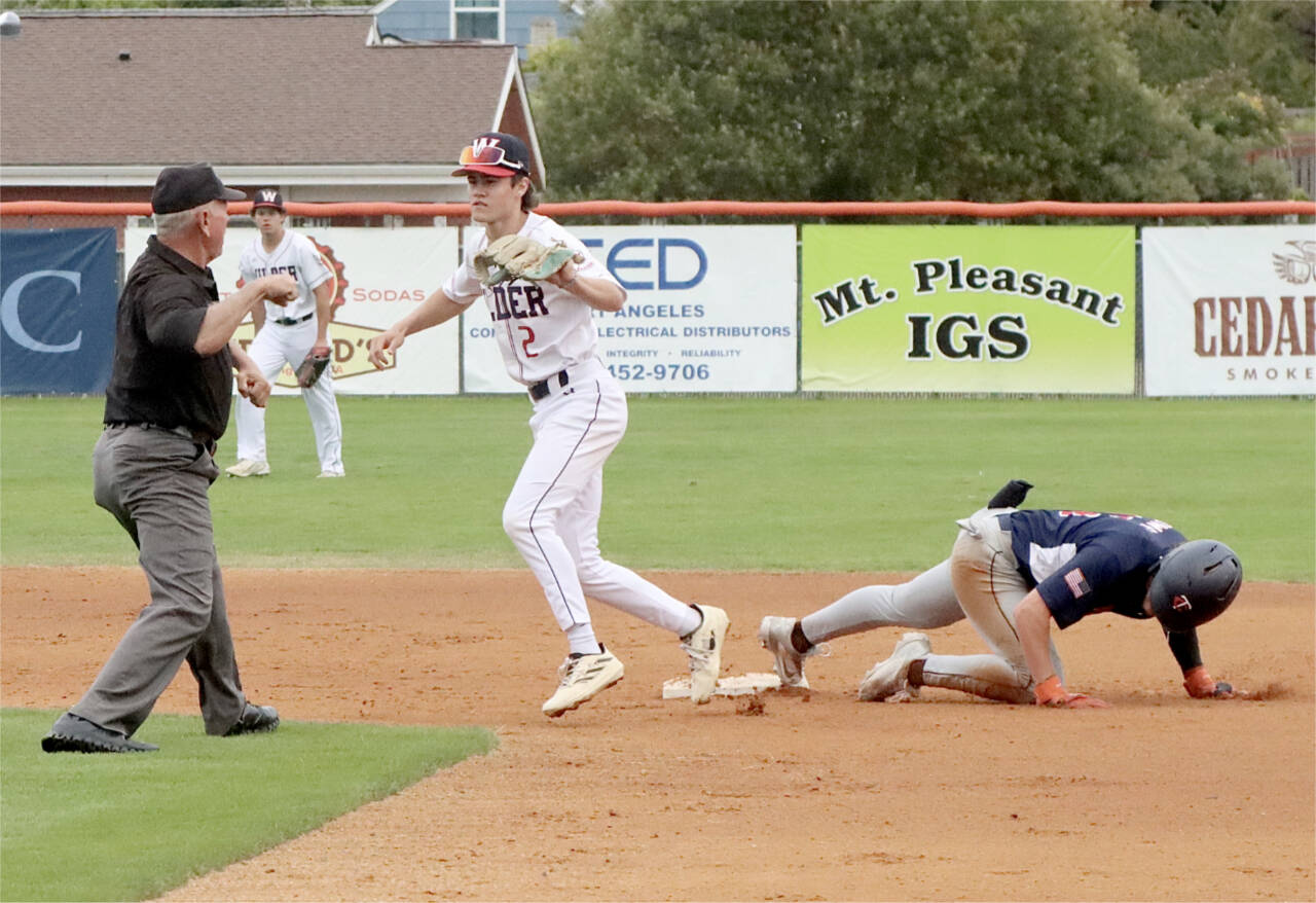 An umpire gives an emphatic out sign as Wilder Senior shortstop Alex Angevine applies a tag to a Twin-Cities Titans player at second base in Sunday night’s AAA state tournament game at Civic Field. (Dave Logan/for Peninsula Daily News)