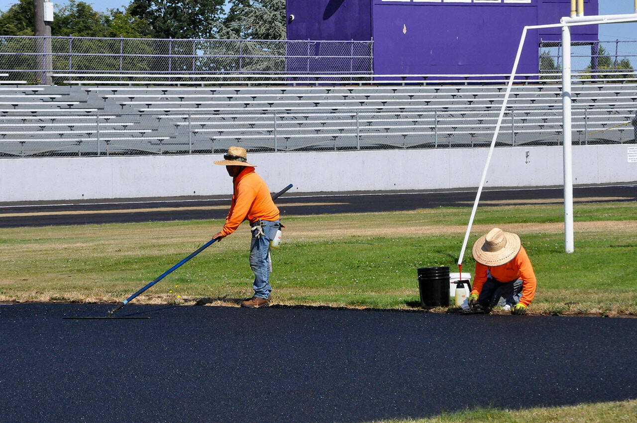 Workers with Beynon Sports of Oregon flatten new material for the high jump area on July 19. (Matthew Nash/Olympic Peninsula News Group)