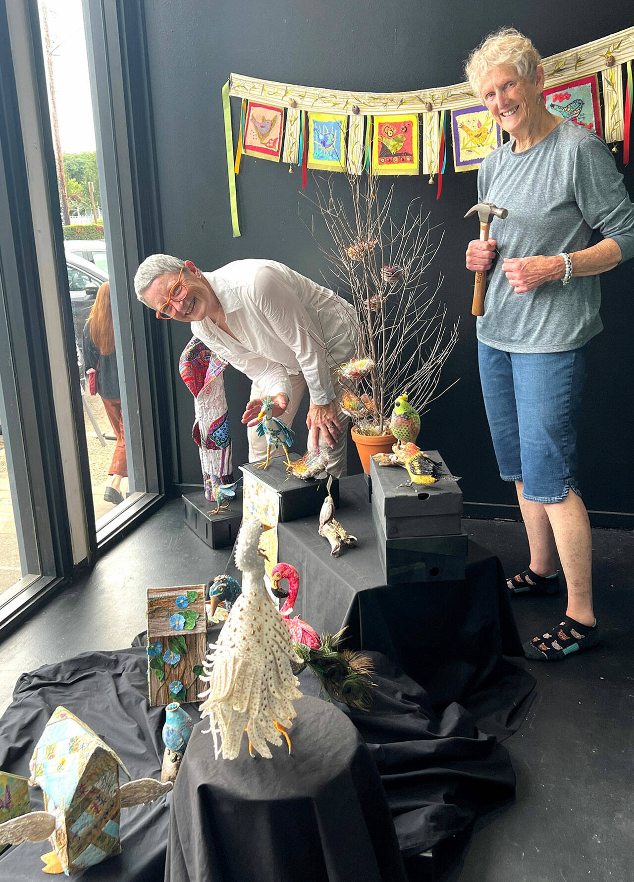 Debra E. Olson, left, and Leslie Dickinson install “Birds of a Feather” in the Fiber Habit walk-by exhibit of Peninsula Fiber Artists, 675 Tyler St. in Uptown Port Townsend.