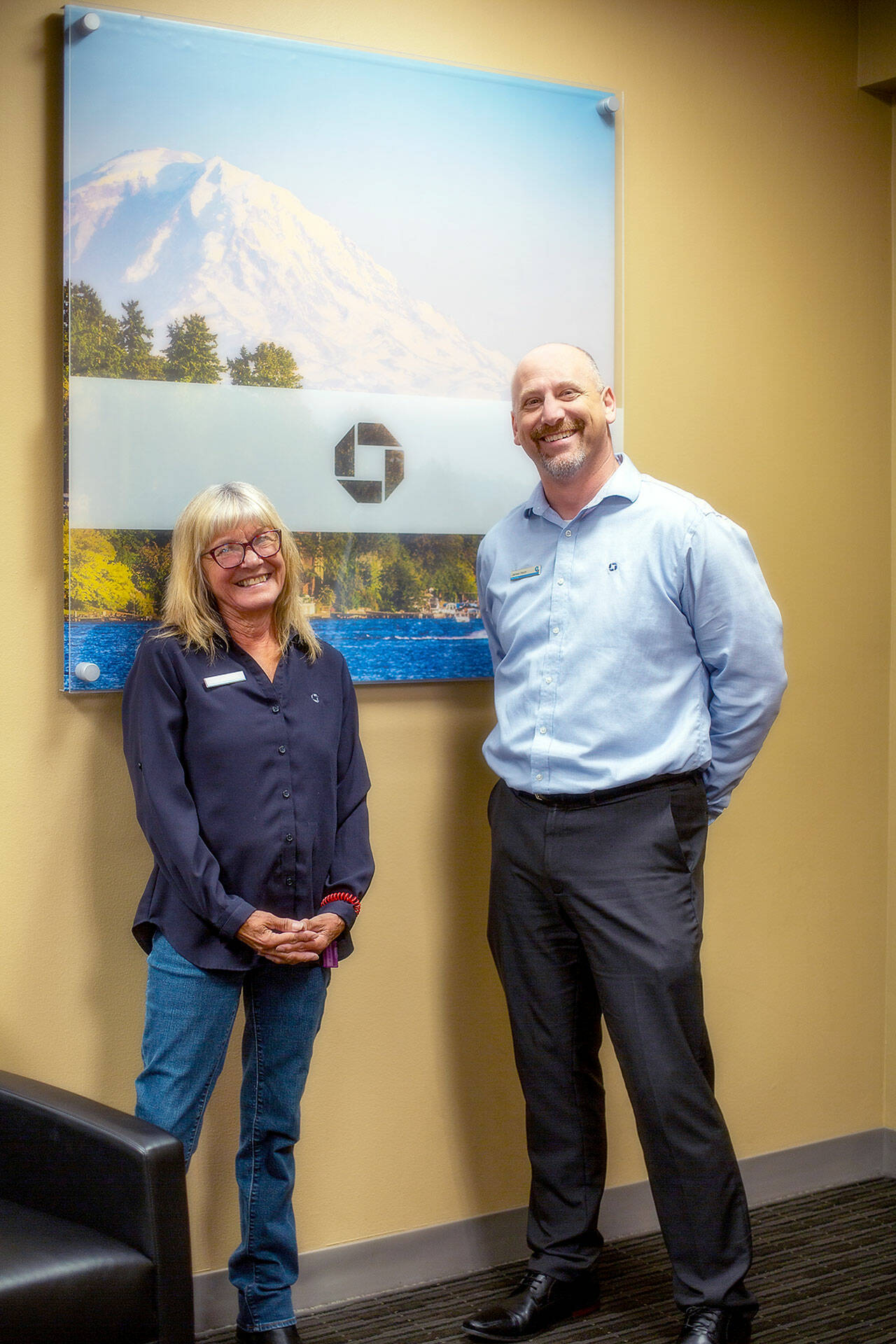 Elva Hulett, left, and James Hoch, Port Angeles Chase Bank branch manager, smiling together, reminiscing about Hulett’s milestone achievement at Chase Bank on Aug. 8. (Christopher Urquia/Peninsula Daily News)