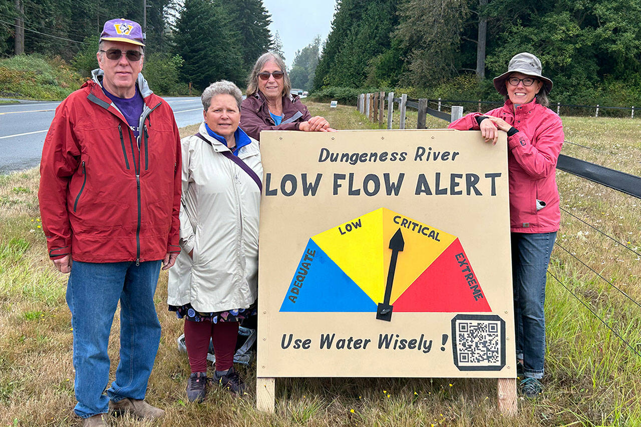 David Brehm, Jeene Hobbs, Barbara VanderWerf and Ann Soule from the Clallam County League of Women Voters stand with a new sign that shows the level of water flow for the Dungeness River. While the river flow was considered critical on Aug. 23, levels improved slightly to “low” flow later that night. The sign, just west of Knutsen Farm Road on Old Olympic Highway, will be updated weekly, organizers said. (Matthew Nash/Olympic Peninsula News Group)