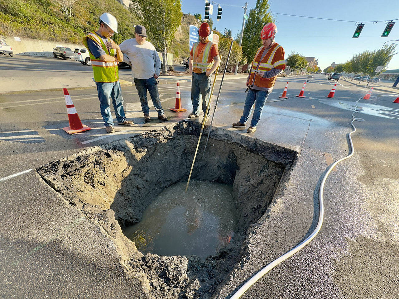 Port Townsend Public Works Director Steve King, left, discusses ways to repair the broken sewer line that developed a sinkhole late Friday night on Water Street at the entrance to the Port Townsend ferry dock, with Talon Cameron of Seaton Construction, Lane Dodson and Adam Fructas. Raw sewage continues to flow through the 70-year-old pipe and partially fills the hole. Plans were to make a temporary fix with a steel plate over the hole until more permanent repairs could be made. (Steve Mullensky/For Peninsula Daily News)