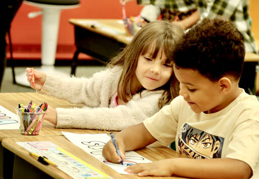 Violet Wilkie looks to see how her classmate Sylas Hall is coloring his name tag, the first chore on the first day of school Tuesday in Danika Johnson’s first-grade classroom at Hamilton Elementary in Port Angeles. (Dave Logan/for Peninsula Daily News)